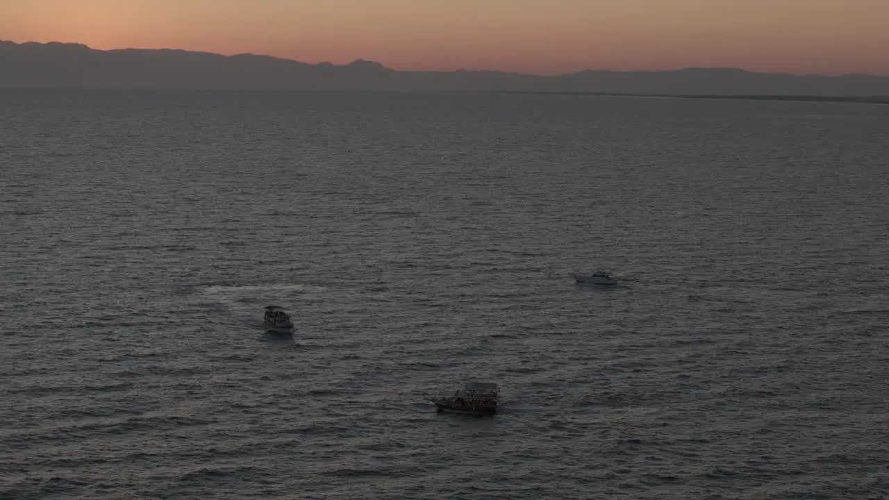 Small boats navigating Mediterranean sea under glowing sunset orange skyline