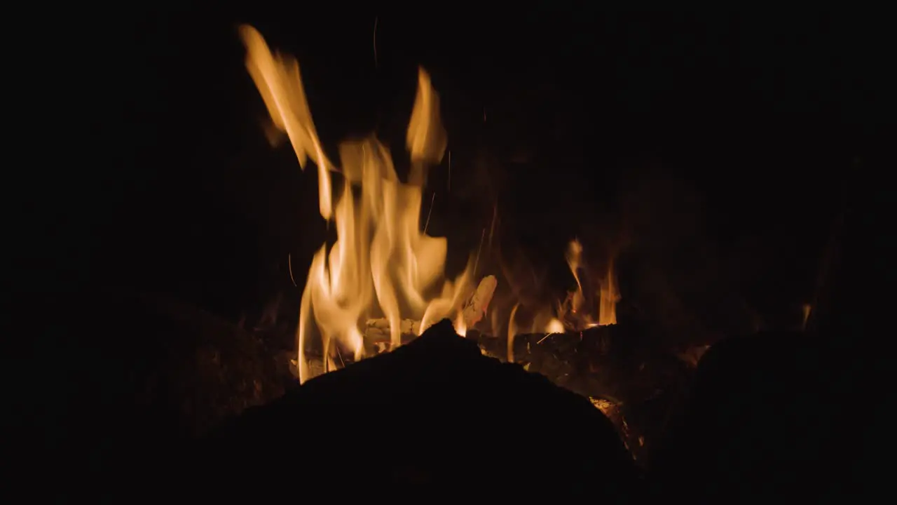 A warm campfire is burning bright at night with the silhouette of rocks in front of it