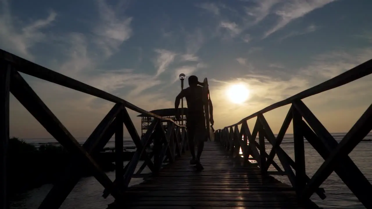 A fit surfer running down the pier at sunset hoping to catch one more wave a slow motion tracking shot