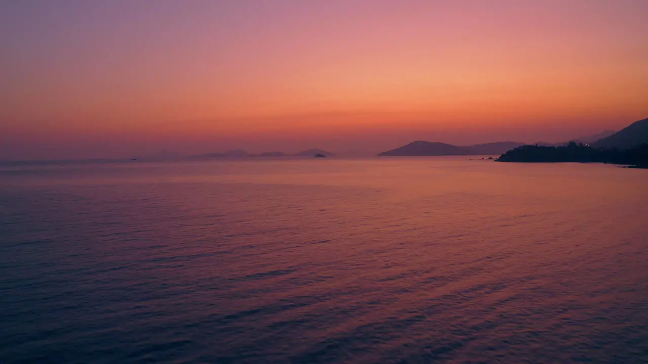 beautiful drone shot of a natural coastline during sunset the light is clear red purple and gold and the sea is reflecting those colors