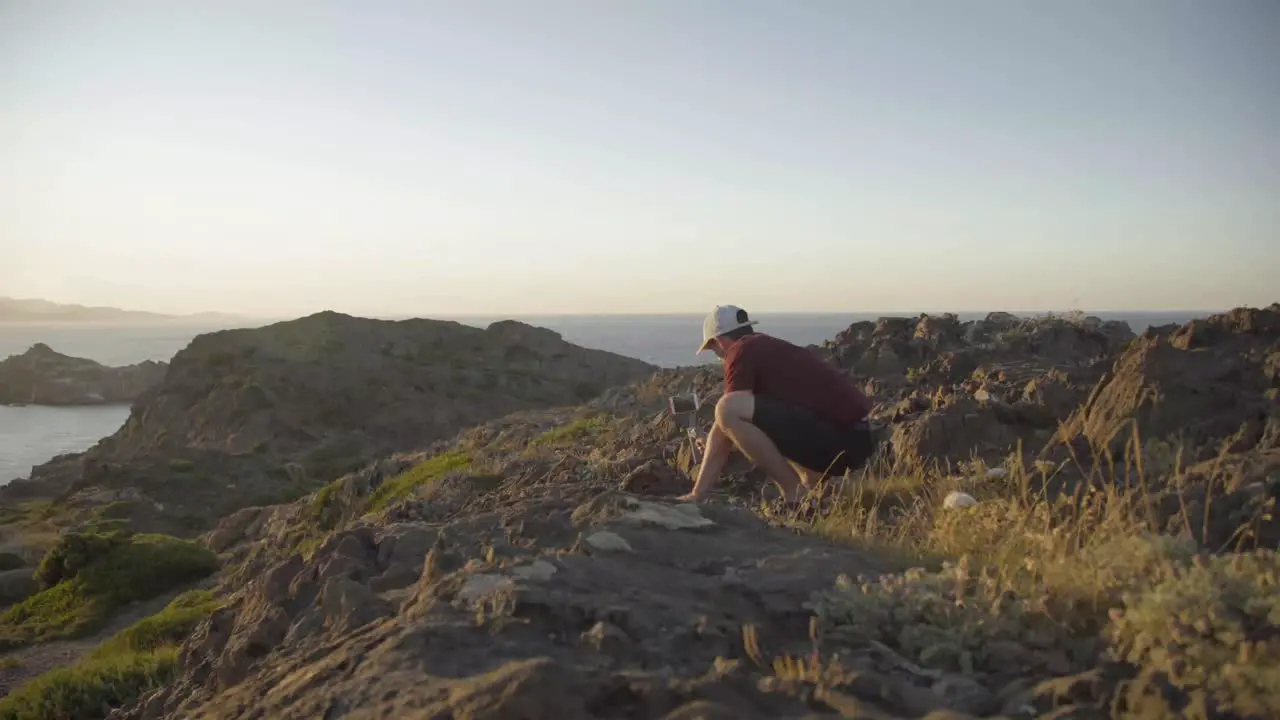 Adventurer filming on the cliff with his phone landscape ocean in the background sunset static shot