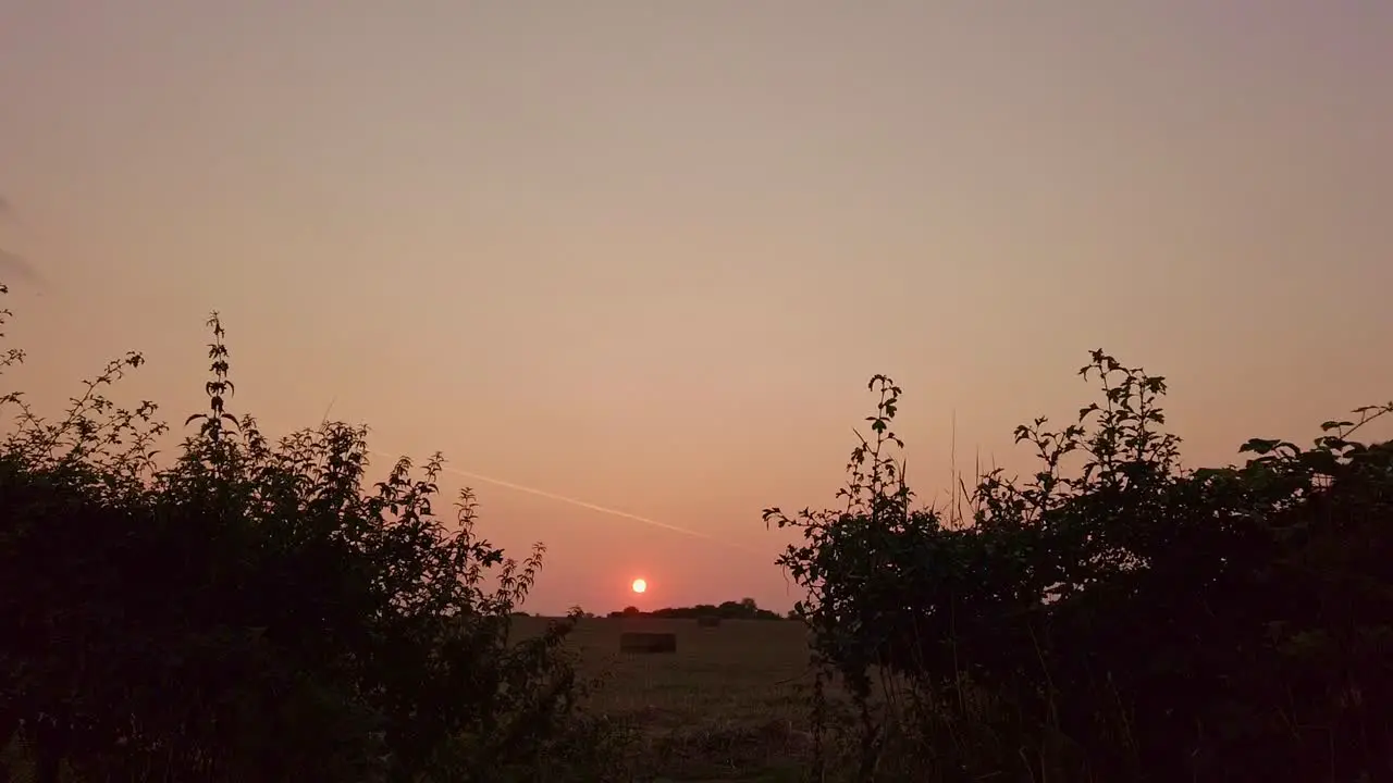 Sliding shot of farm field at dusk looking into a sunset