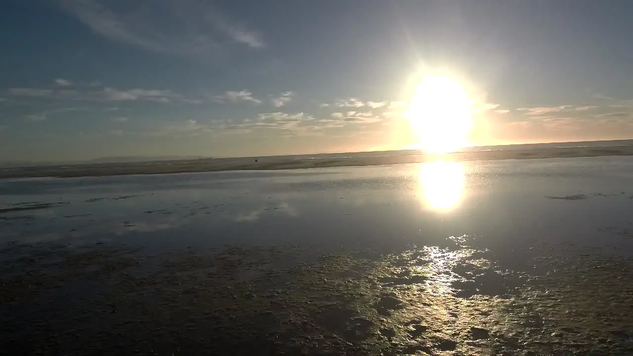 Left to right tracking shot on a beach just above lagoon with sunset in the background