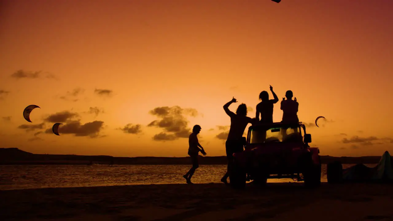 Kiteboarder jumps in front of cheering friends silhouettes against sunset sky