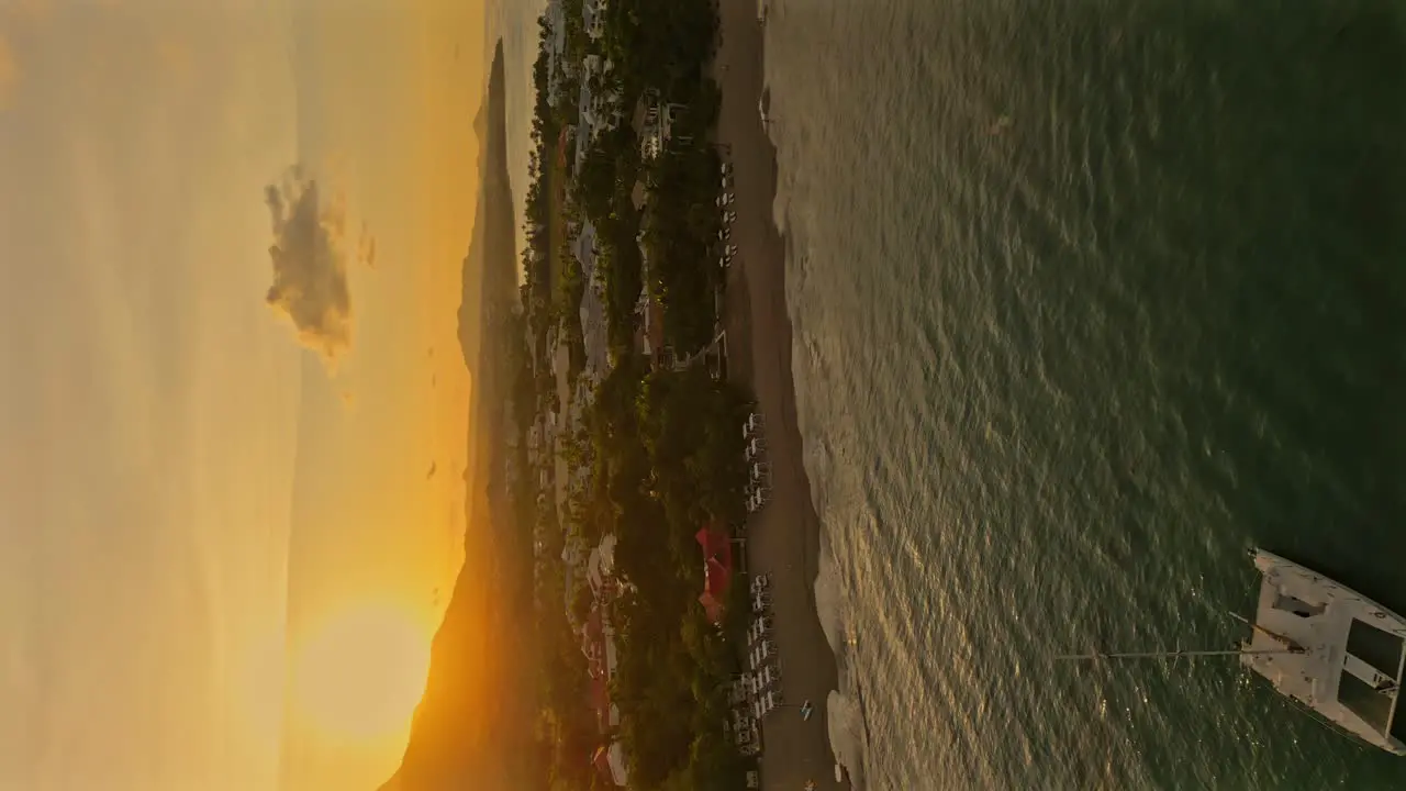 Aerial approaching shot of anchored Catamaran at bay of Playa Dorada City during golden sunset vertical shot