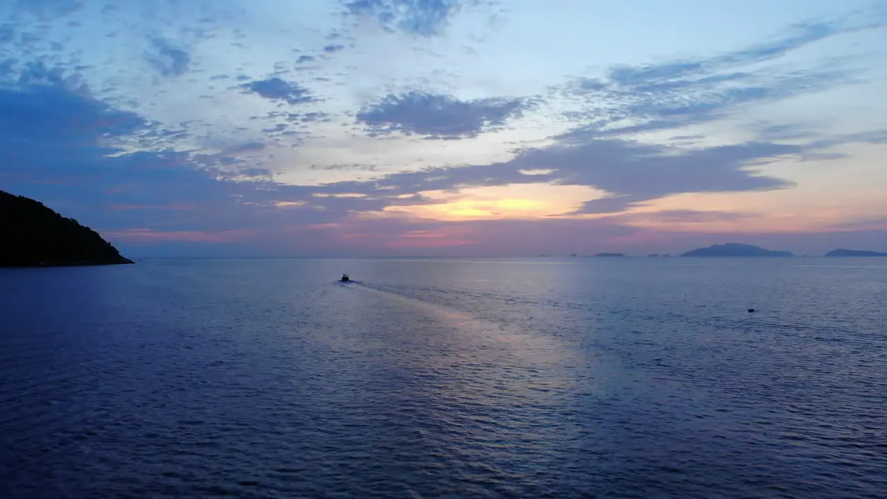 Aerial view of the ocean with a boat rocks and a colorfull sunset