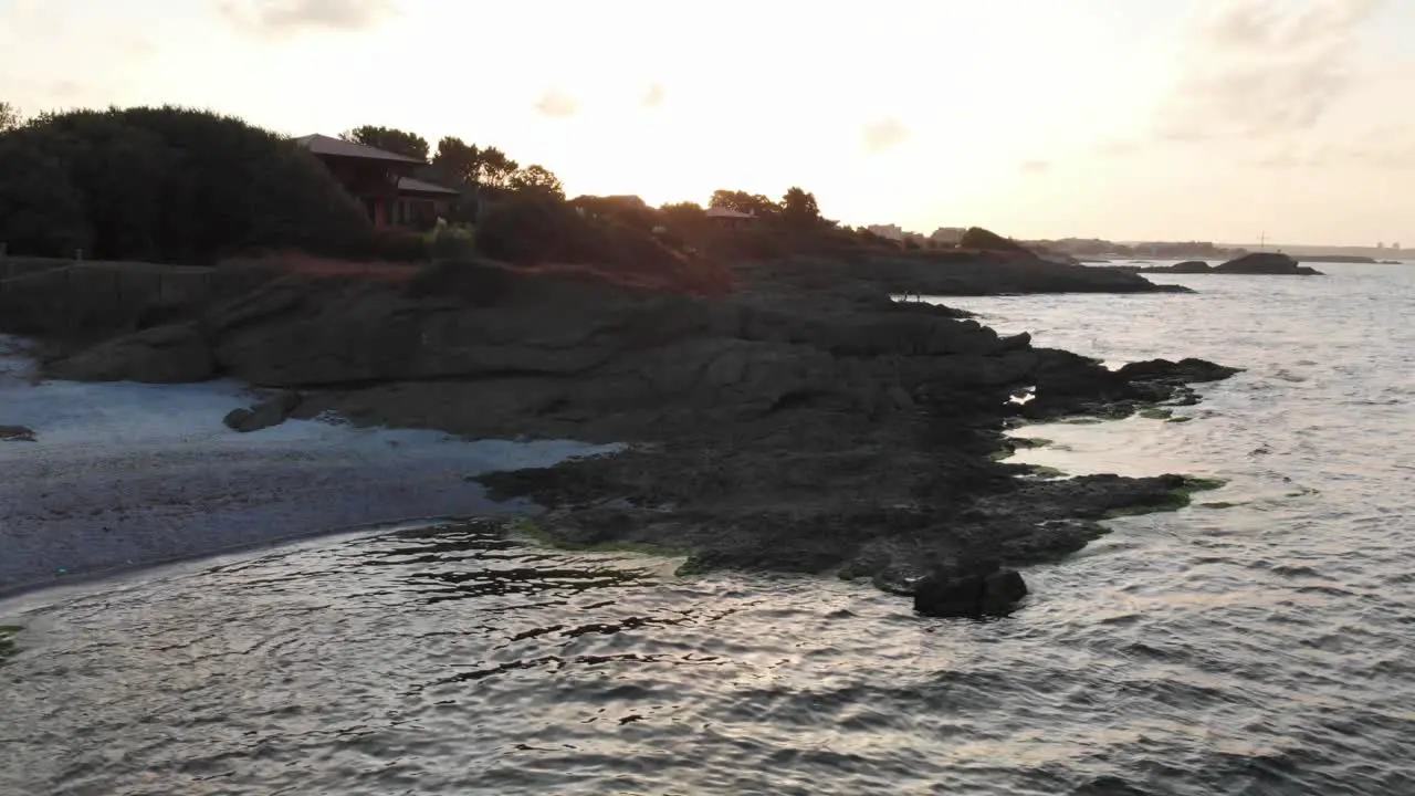 Aerial panning shot around houses on rocky seashore at sunset