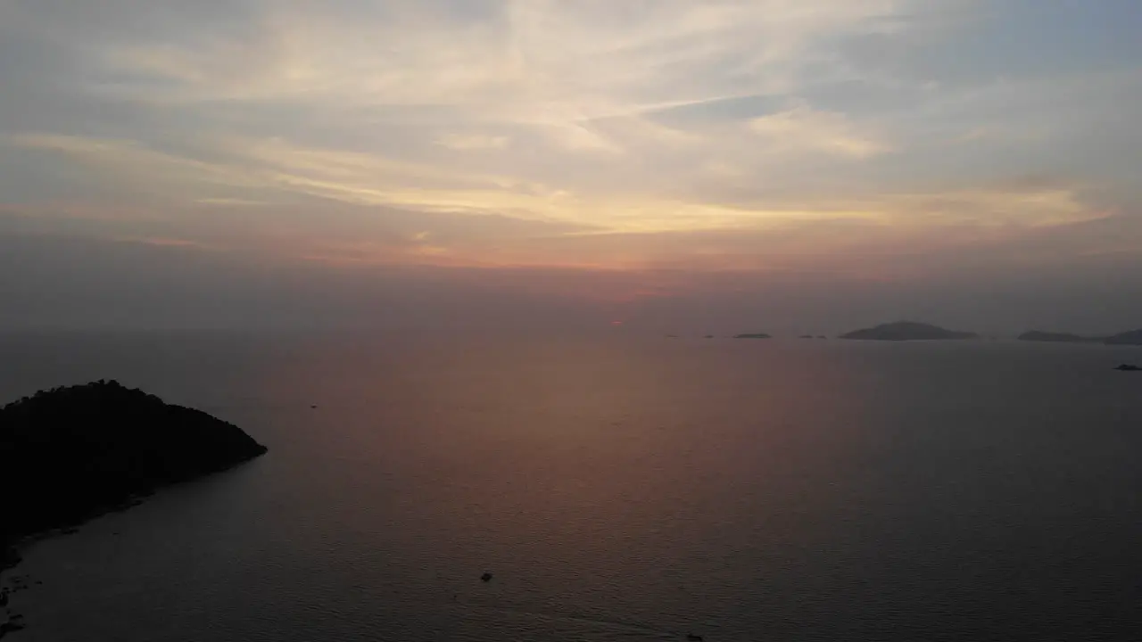 Aerial view of the ocean on a sunset with boats and mountains in the background