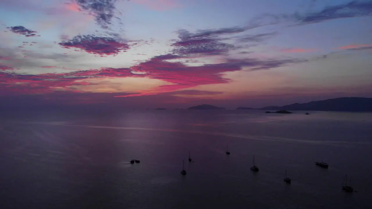 Aerial view of a colorful sunset over the ocean with boats and mountains in the background