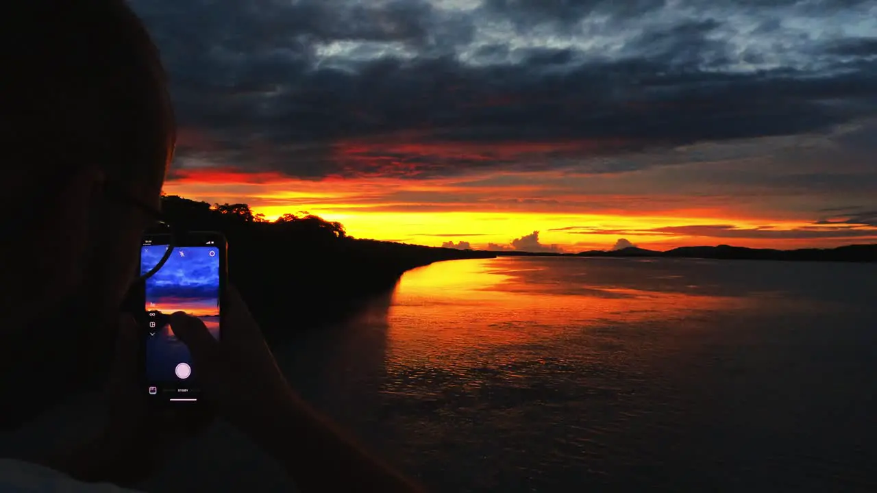 Young man taking a picture of the sunset in Costa Rica with his instagram app on his phone