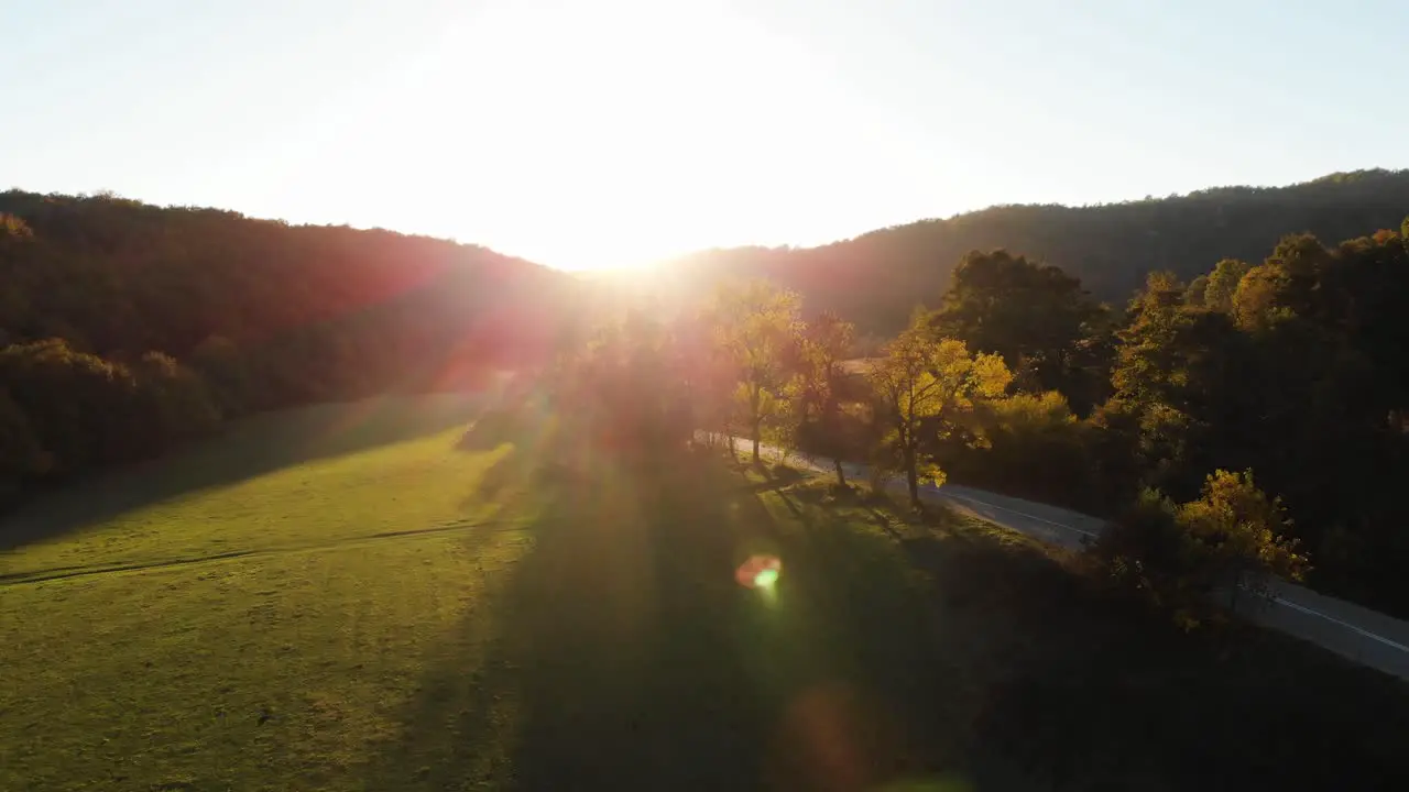 Aerial epic drone shot of sun rays in grass field surrounded by forest at sunset-2