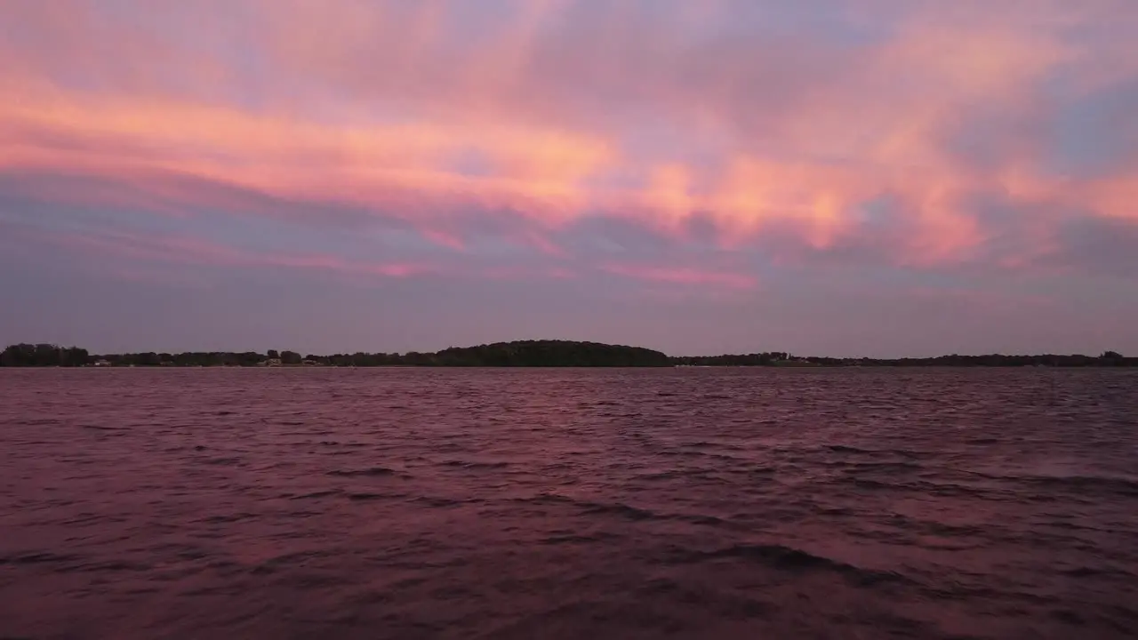 Cinematic drone view over a lake showing a pink blue and white sky with a forest in the background