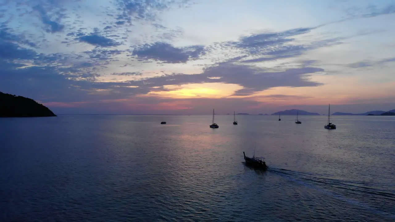 A Thai tale boat sailing towards the sunset with other boats anchored