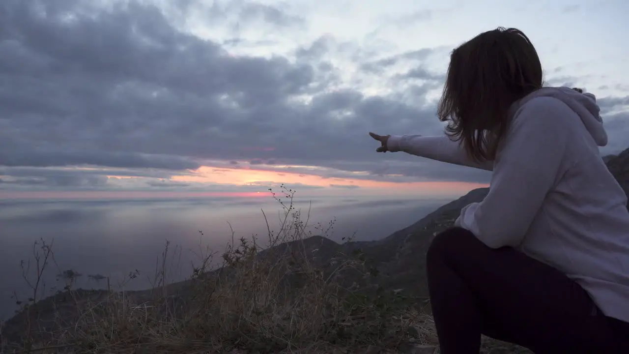 Girl squat on a high cliff and watch the sunset through cloudy sky over Adriatic sea-2