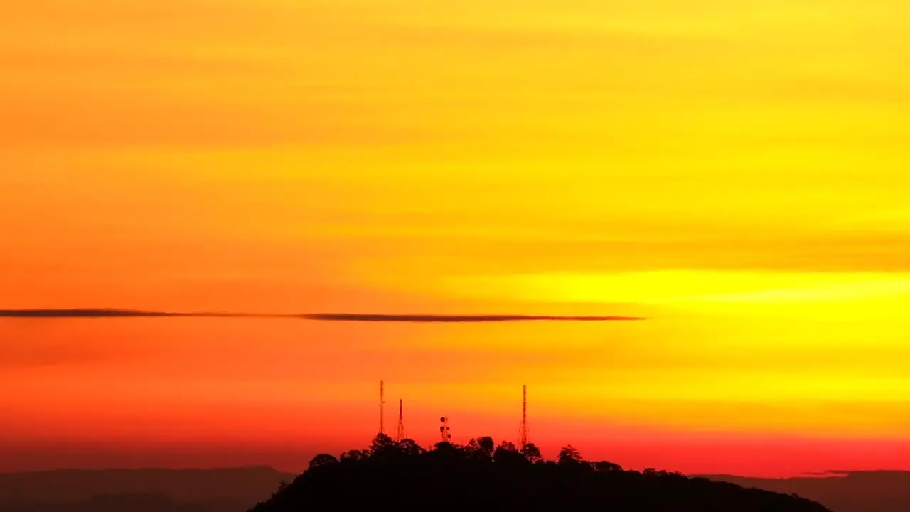 Slow tilt down on silhouette of radio communications towers against vibrant orange sunset