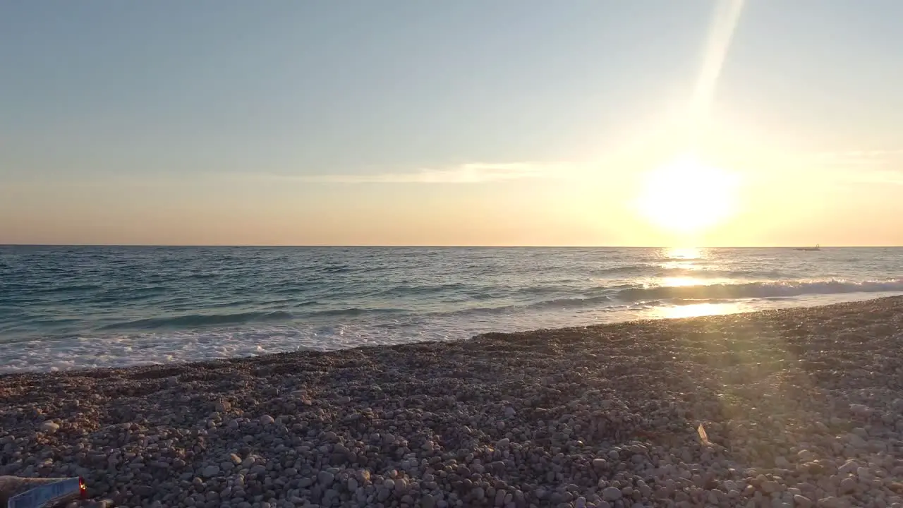 Slow motion pan over trash thrown away on beach at ocean during sunset