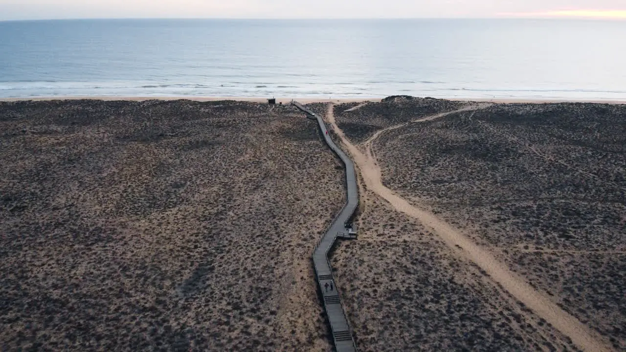 An aerial perspective captures the cinematic beauty of Portugal's coastal landscape featuring a walking pathway and a solitary road winding through a desolate terrain to water surface