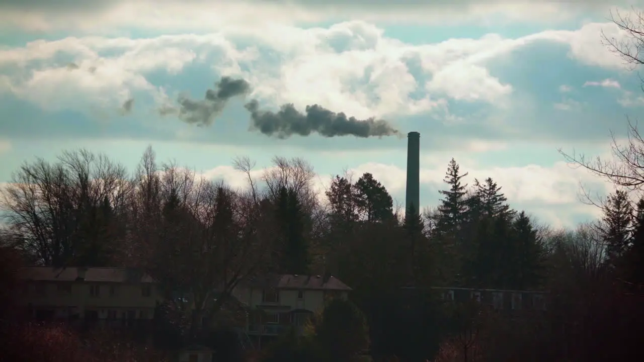 Wide angle of a smoke stack spewing dark thick smoke into the sky on a beautiful day