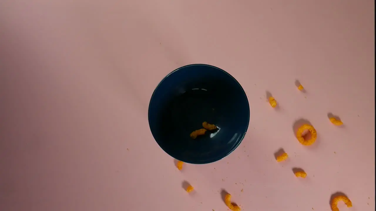 Top view clip of cheese rings falling and scattering around a blue ceramic bowl