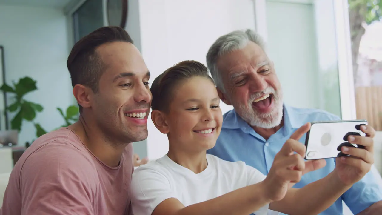 Multi-Generation Male Hispanic Family On Sofa At Home Posing For Selfie On Mobile Phone