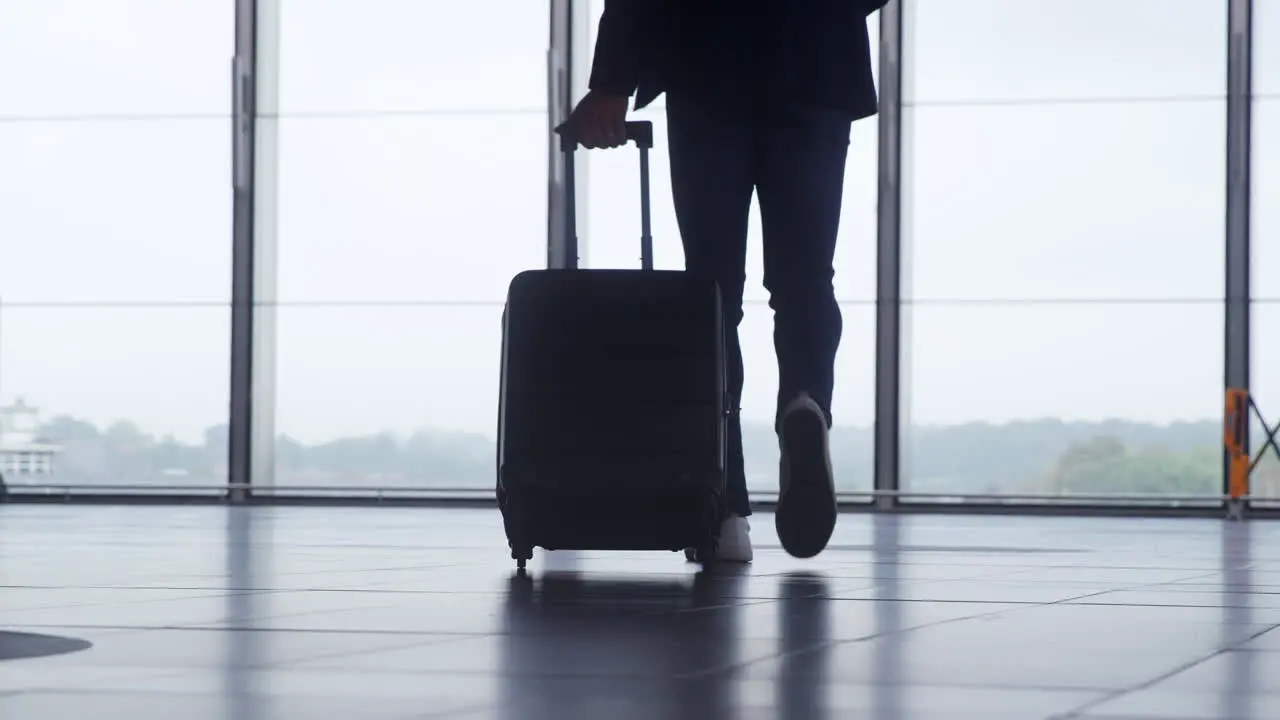 Close Up Of Businessman Wheeling Suitcase Across Concourse At Railway Station With Mobile Phone