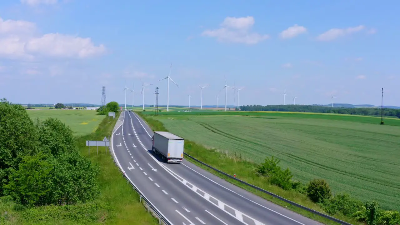 Large White Transport Truck driving on a country road with huge ecological Wind Farm in background