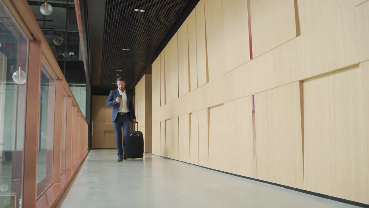 A Young Businessman With Beard In Blue Suit Walks Through A Hallway Carrying A Trolley 1