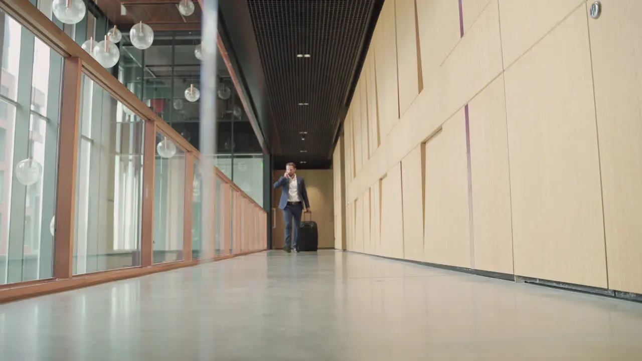 A Young Businessman With Beard In Blue Suit Walks Through A Hallway Carrying A Trolley