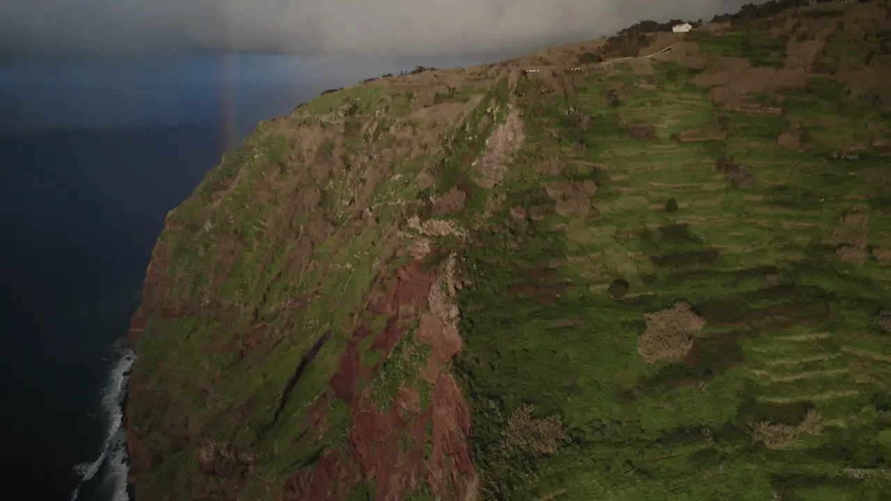 Aerial view with drone of rugged cliffs beside the ocean with a rainbow and waves at Madeira