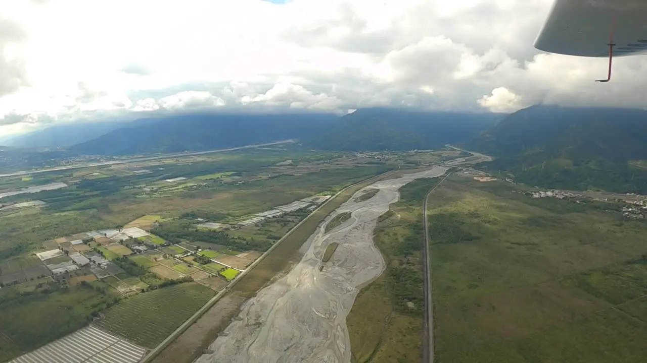 Flying over dried up river bed near farm land and mountains