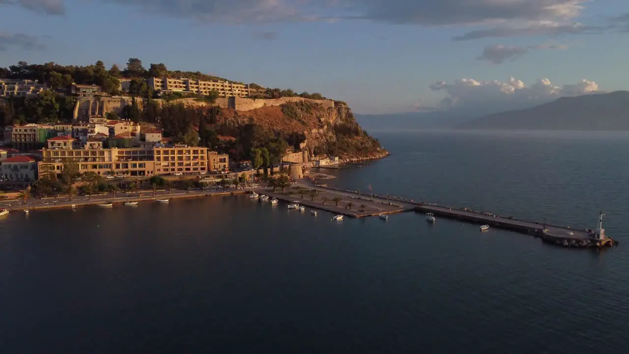 Aerial view of the small Mediterranean town of Nauplio in the Peloponnese region of Greece during a cloudy afternoon with a lighthouse on the right side | 4K