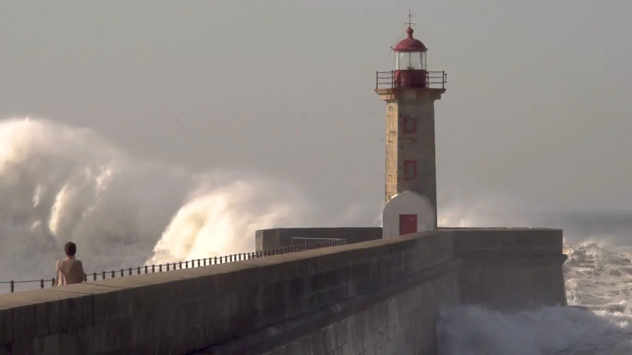 ocean big waves crash over the lighthouse with a person in the foreground