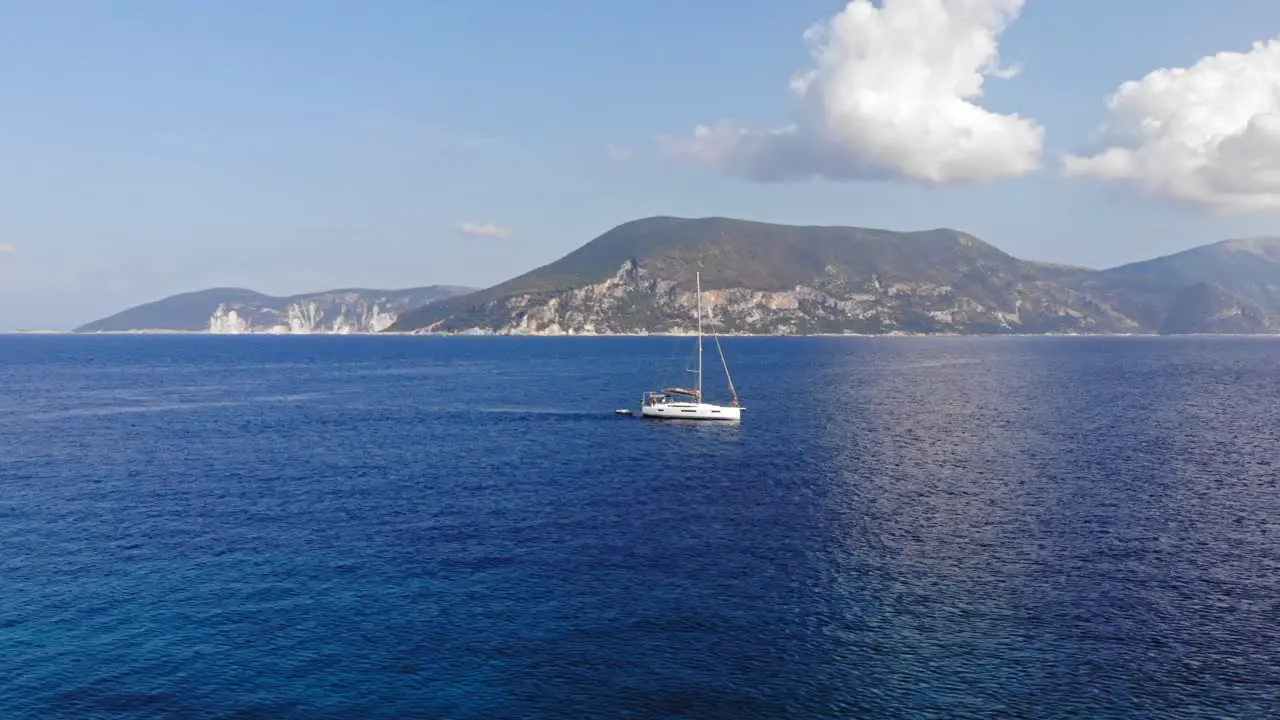 Boat Sailing Through The Blue Ocean On A Cloudy Day Overlooking The Mountainside Of Paralia Emplisi Kefalonia Greece -Lateral Aerial Shot