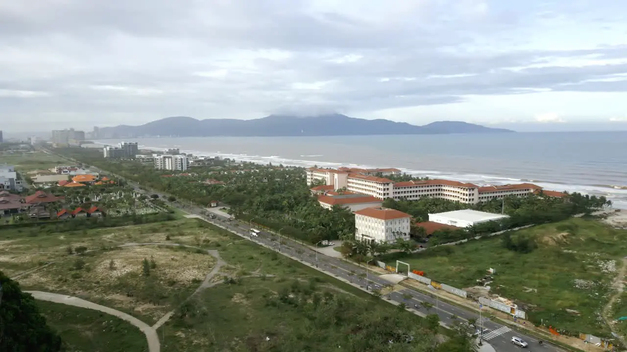 Flyover from the mountains to Ha My Beach on a cloudy day with wave hitting the shore in Da nang Vietnam