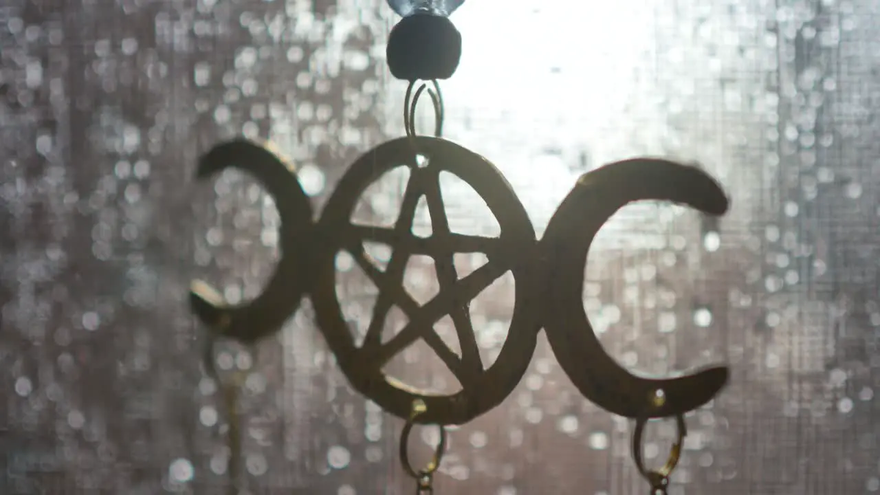 Close-up of a moon pentagram decoration hanging in a screen window on a rainy day