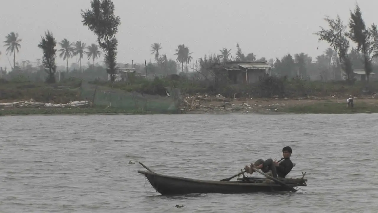 A young boy is sailing a boat in a river rowing with his feet on the Mekong River in Vietnam