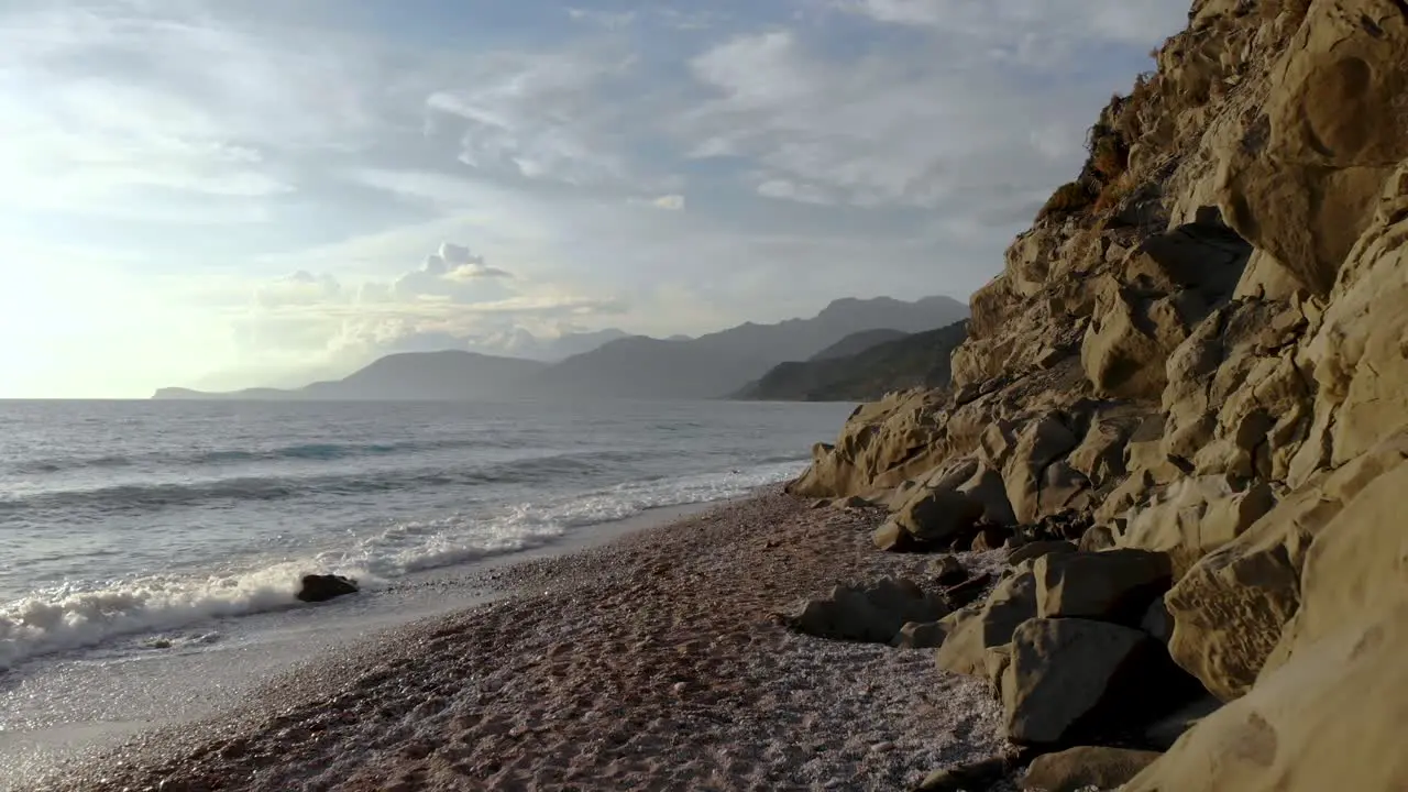 Dramatic seascape with rocky seaside and pebbles beach splashed by sea waves on a cloudy day in Mediterranean