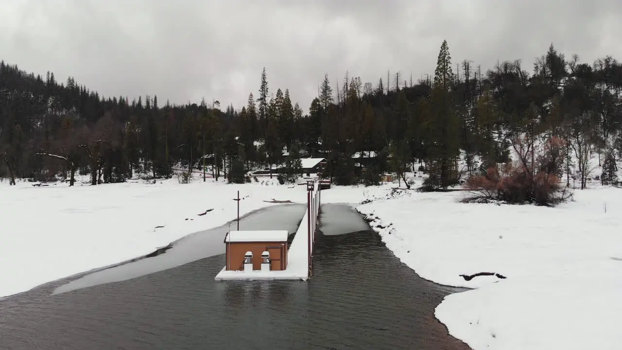 Aerial flyover shot of dock covered in snow on a frozen lake