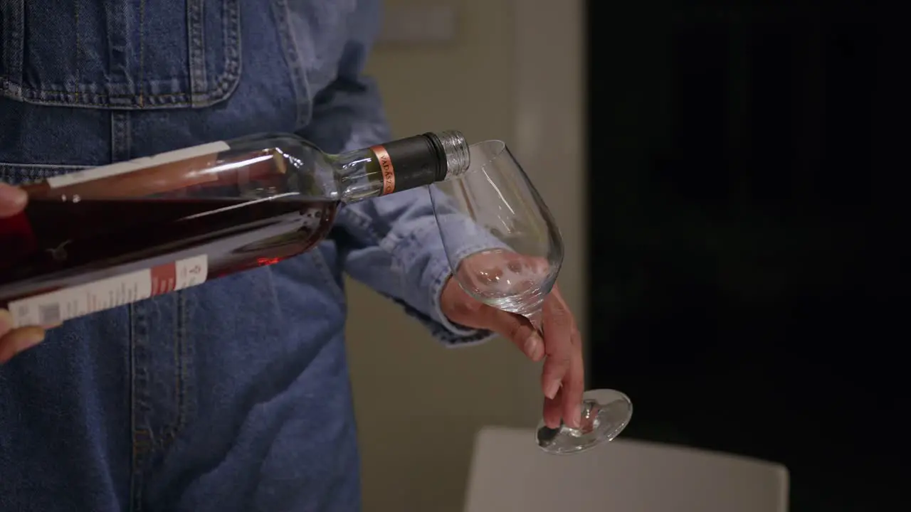 Woman wearing denim clothes pours red wine into wine glass dinner party at home evening alcohol consumption hands close-up shot health wine tasting drinking sober celebration predrinks