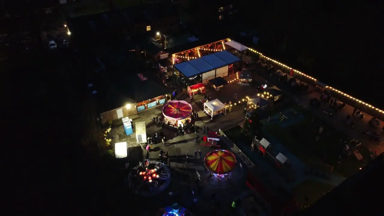 Illuminated fairground festival in neighbourhood pub car park at night aerial view