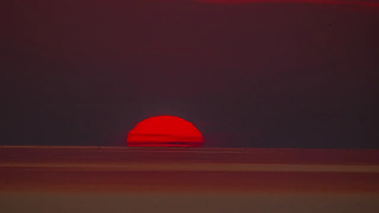 The orange sun dips beyond the ocean's horizon at sunset time lapse