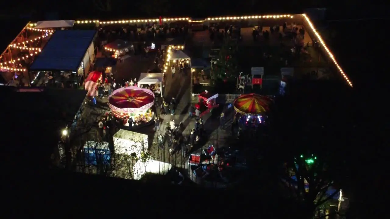 Illuminated colourful Christmas fairground festival in neighbourhood car park at night aerial view