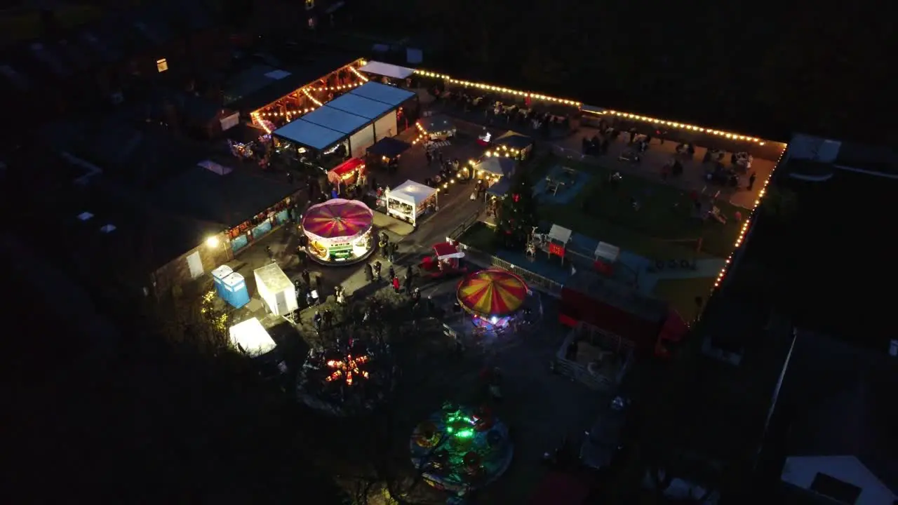 Illuminated Christmas fairground festival in neighbourhood car park at night aerial circling view