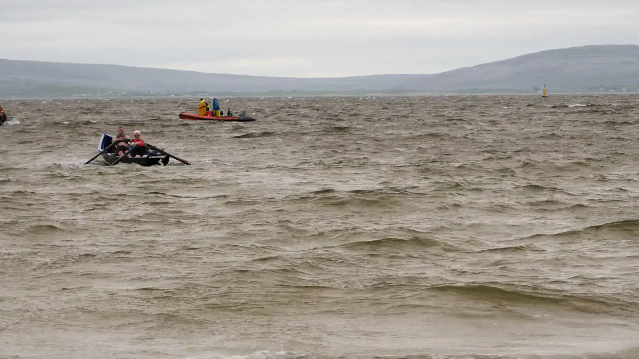 Pair of paddlers row currach boat out to open ocean sea on grey stormy day