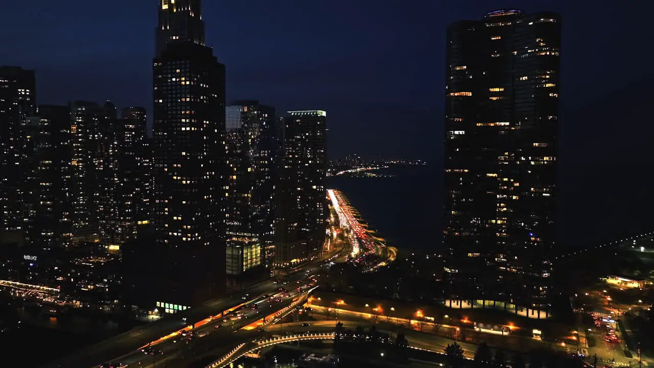 Aerial tracking shot of traffic in middle of skyscrapers on the illuminated lakefront of Chicago