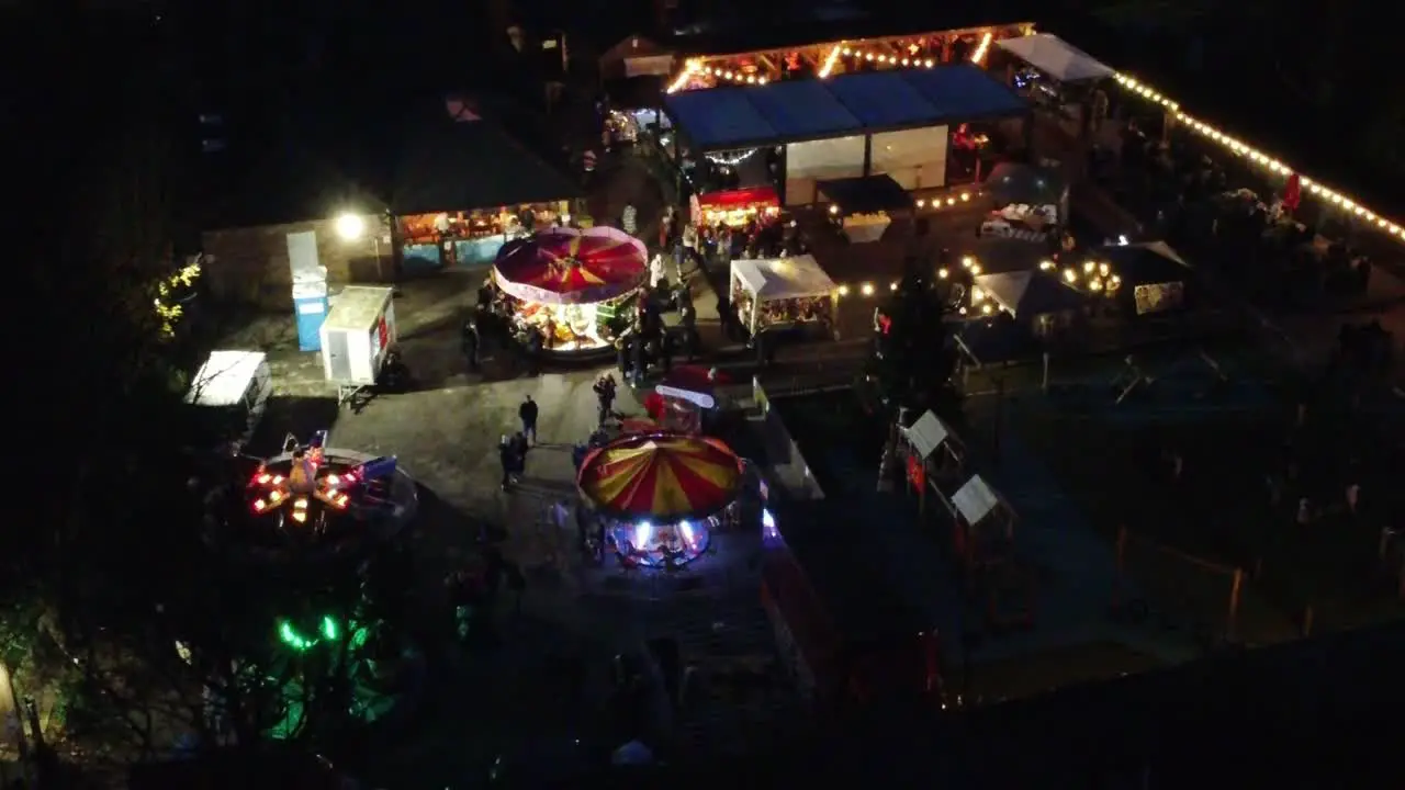 Illuminated Christmas fairground festival rides in neighbourhood car park at night aerial view