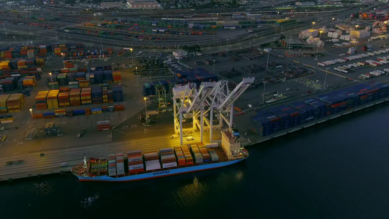 The glowing lights from a crane and ship at the Port of Oakland at nighttime aerial parallax tilt down view