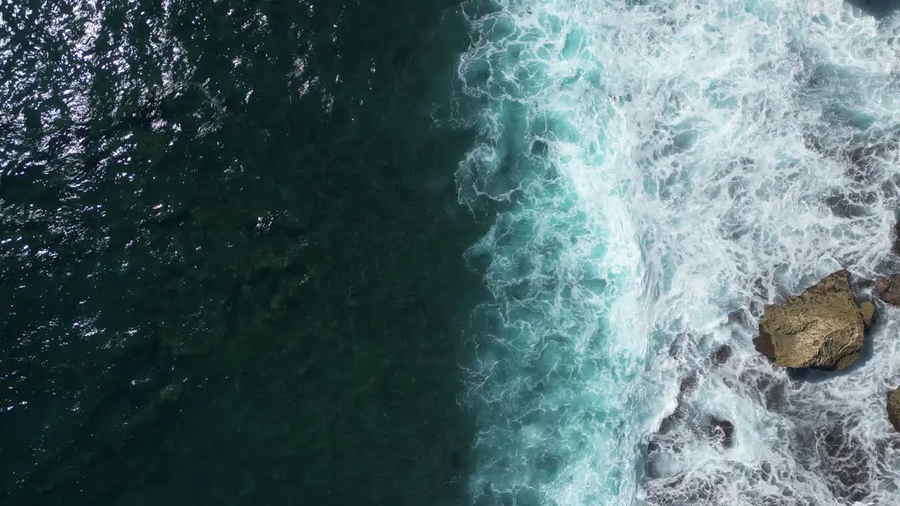 Birds eye view of waves hitting rocks in the South of Bali Indonesia on a sunny afternoon