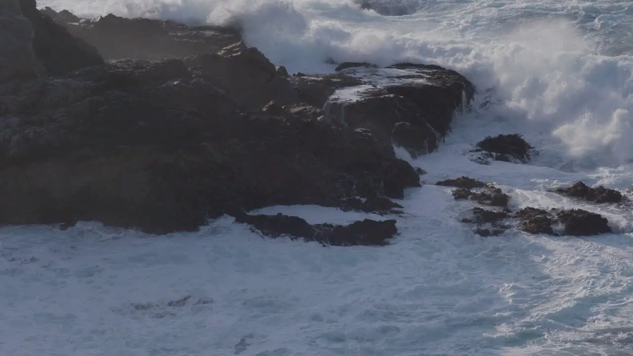 Stationary shot of waves crashing against the massive boulder on a Big Sur California Beach