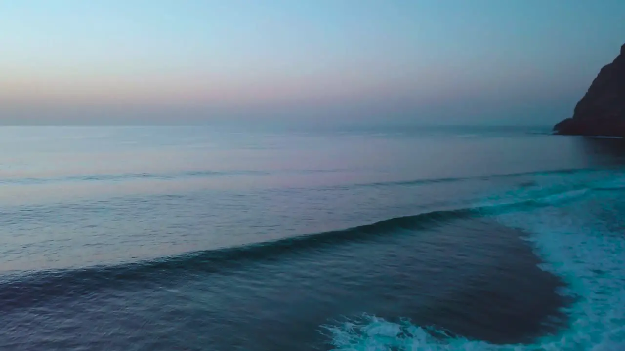 Aerial drone shot of small breaking waves along mountainous coastline with sunset afterglow